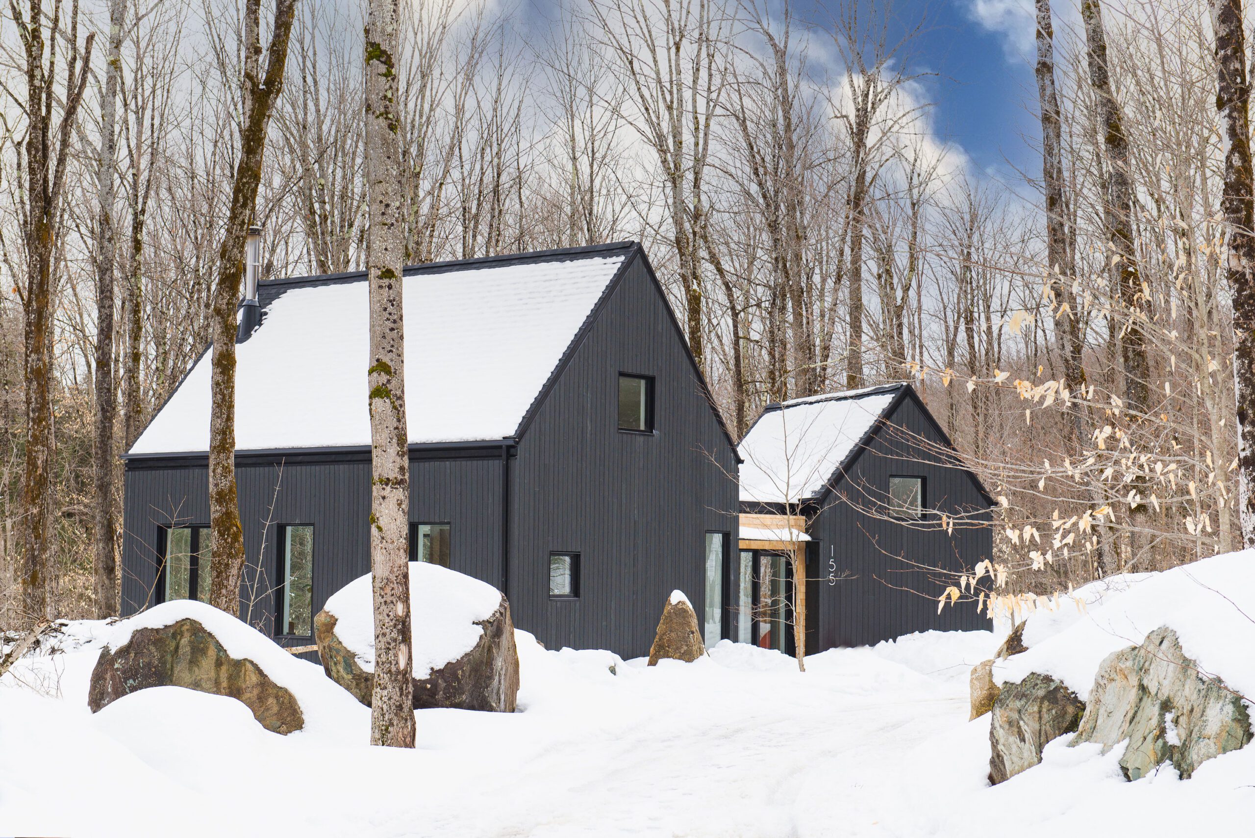 Façade noire élégante et lignes épurées : une maison contemporaine nichée au cœur de la forêt enneigée.