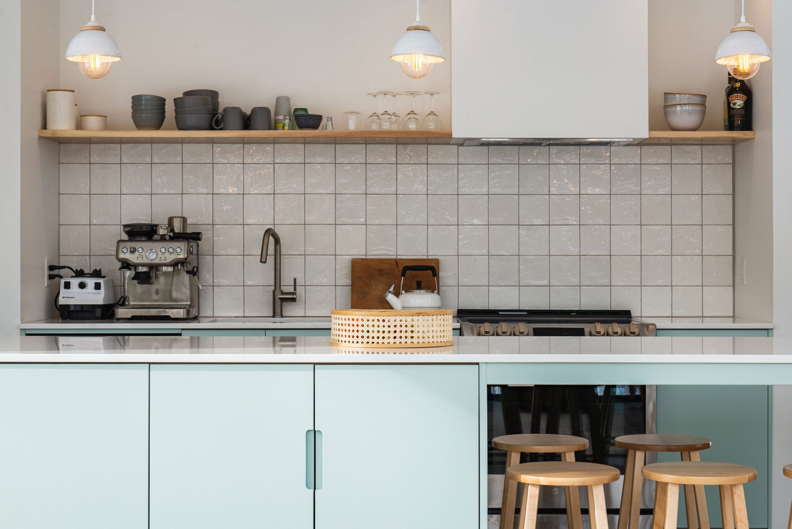 Cuisine moderne avec armoires vert sauge, comptoir blanc, dosseret en carreaux brillants, et coin café avec machine espresso